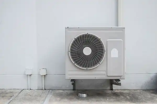 A white outdoor air conditioning unit, part of a recent heat pump installation in Beltsville, MD, is mounted on a wall above a concrete surface.