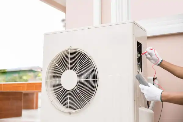 A person wearing white gloves uses a multimeter to check the wiring of an outdoor air conditioning unit during heat pump maintenance in Beltsville MD.
