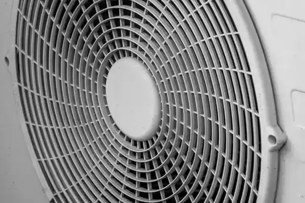 Close-up view of a circular, white plastic fan grille with a geometric grid pattern, commonly seen in Heat Pump Repair systems in Beltsville, MD.