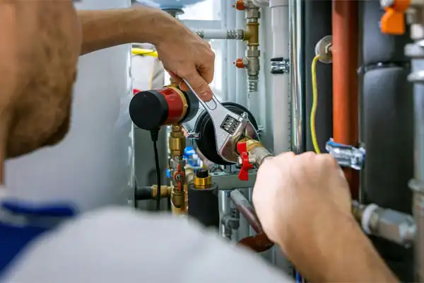 A plumber in Beltsville, MD uses a wrench to tighten a pipe fitting on a complex plumbing system with valves and pipes during a humidifier installation.