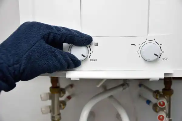 A gloved hand adjusts the temperature setting on a white tankless water heater with visible hoses and control knobs labeled "High," highlighting maintenance in Beltsville MD.