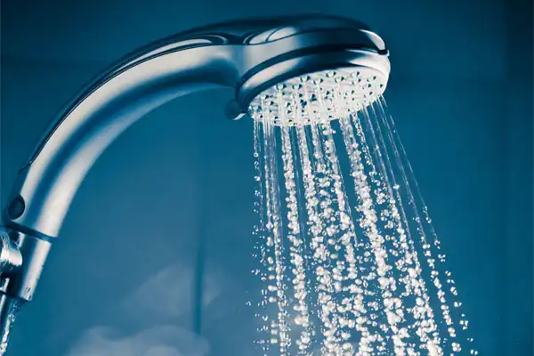 Close-up of a showerhead with water spraying down in multiple streams against a blue background, highlighting the reliable flow you can expect after expert tankless water heater repair in Beltsville, MD.