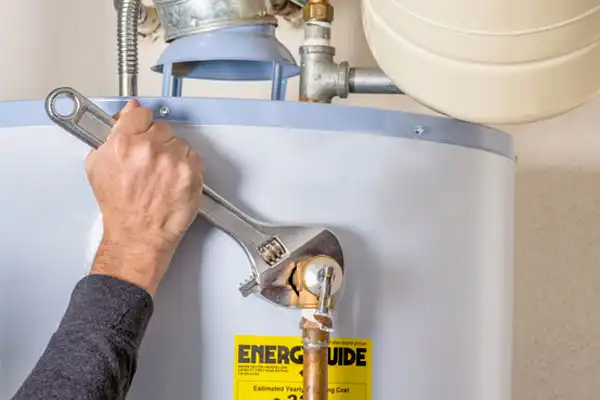 A person in Beltsville, MD uses a wrench to perform water heater repair, tightening a pipe on a unit with an EnergyGuide label.