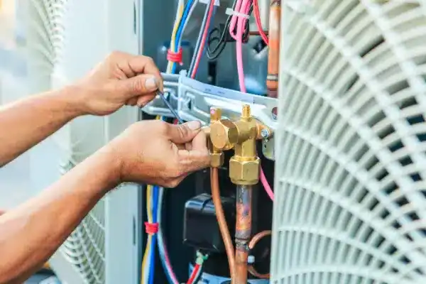 A technician in Beltsville is using a hand tool to adjust wiring and components inside an HVAC unit during air conditioning maintenance, with visible copper pipes and electrical cables.