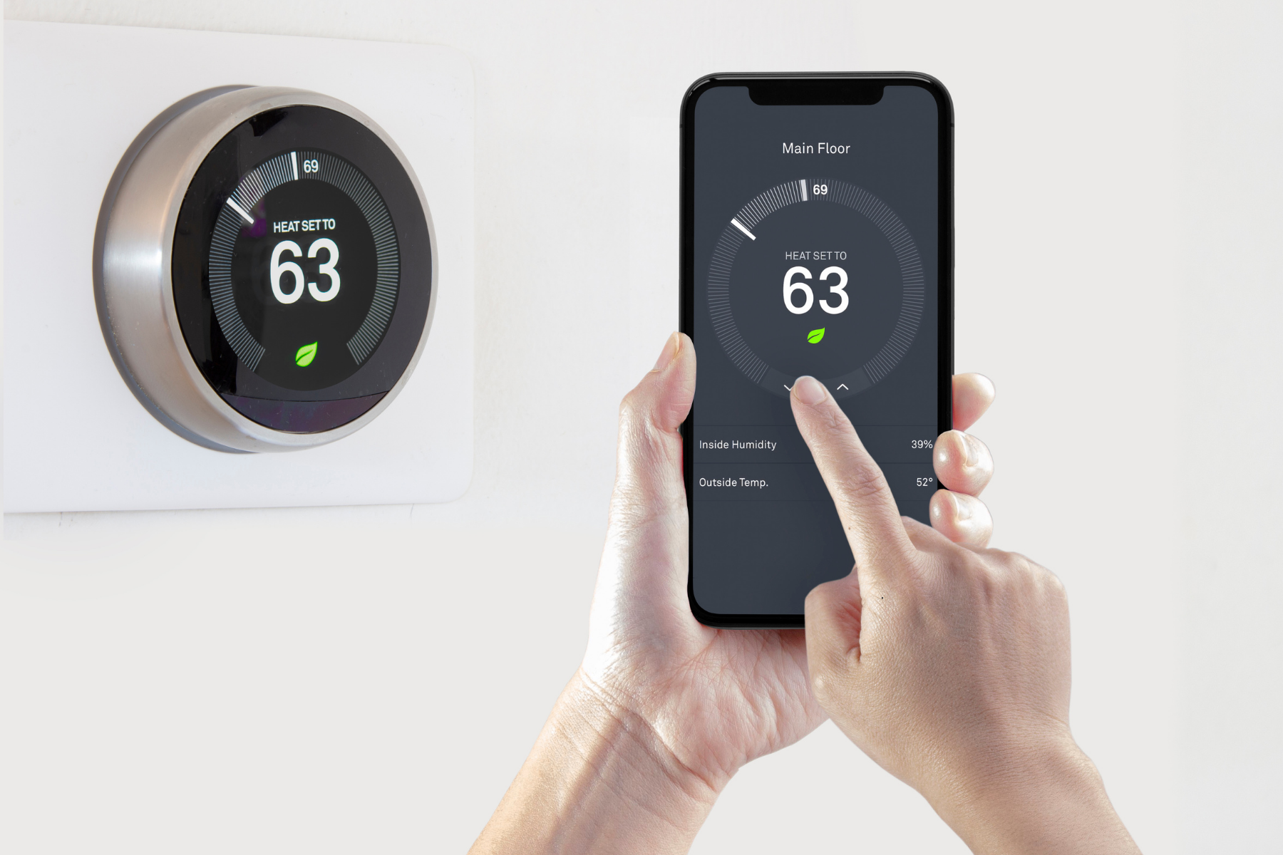 A person adjusts a smart thermostat set to 63 degrees using a smartphone app, with both the wall device and phone displaying the same information—demonstrating effective thermostat troubleshooting and ensuring there are no thermostat problems.