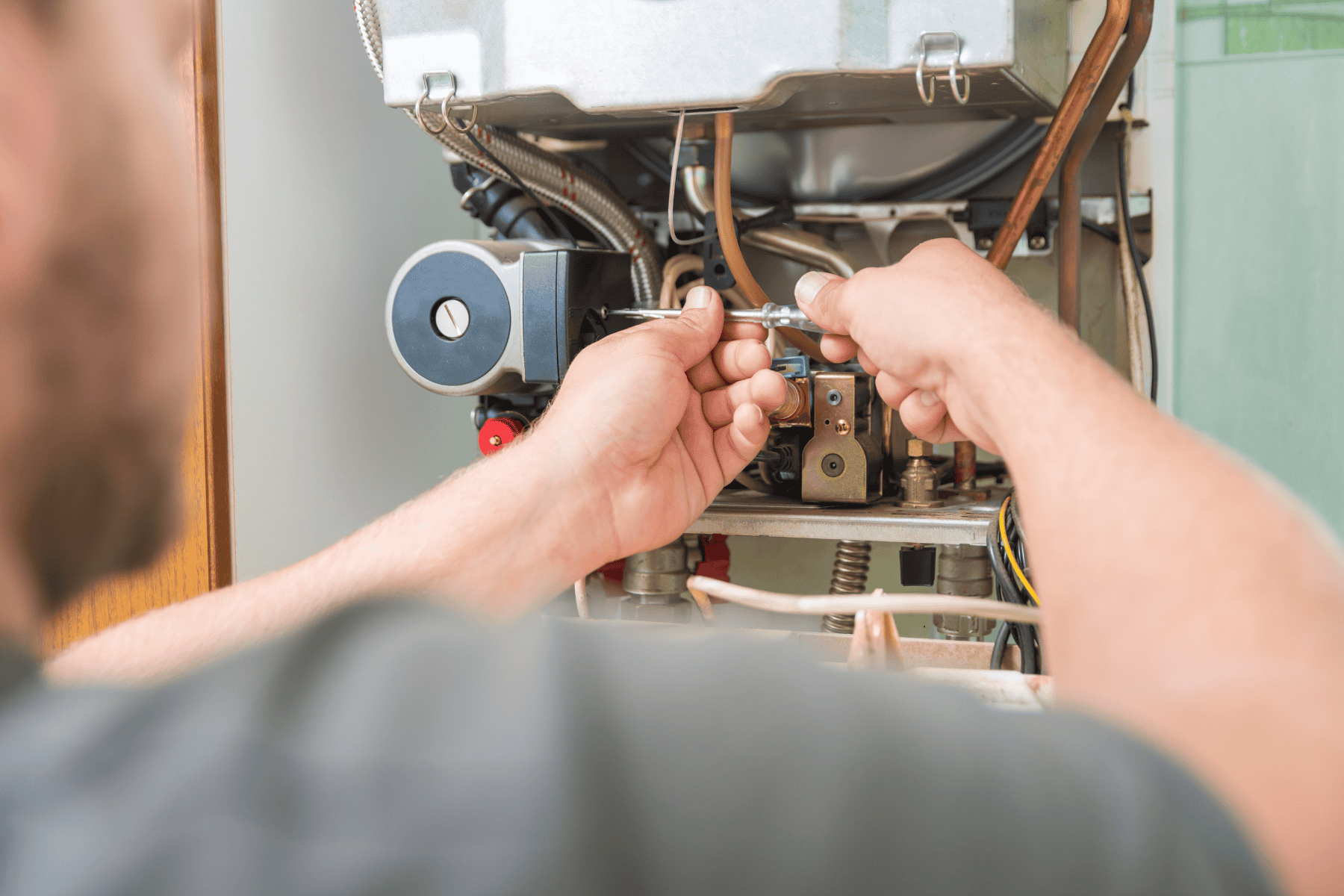 A person uses a wrench to adjust or repair the internal components of a wall-mounted gas boiler, possibly addressing issues related to a failing furnace capacitor.